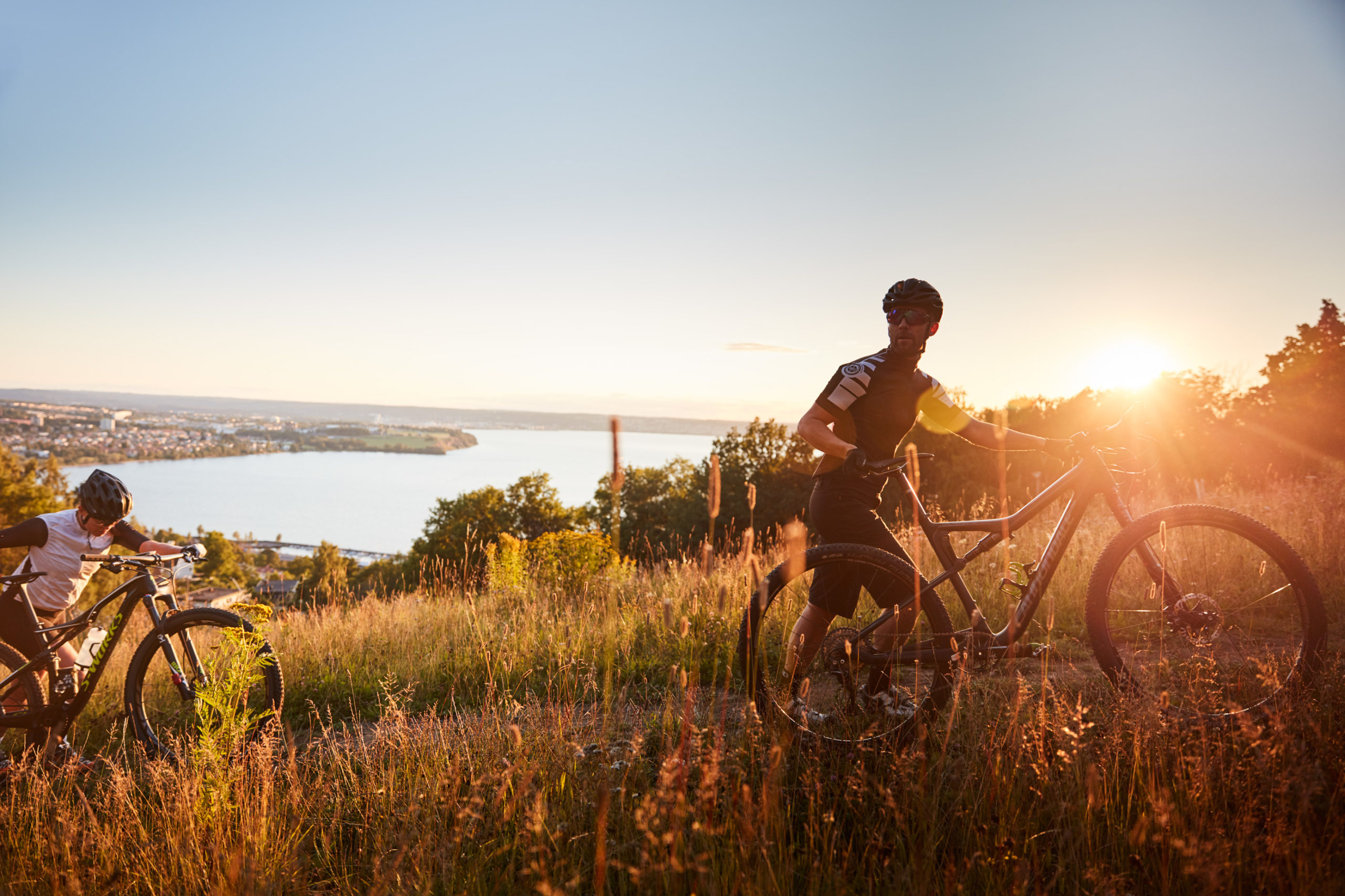 Två mountainbikecyklister leder sina cyklar i uppförsbacke med Vättern i bakgrunden