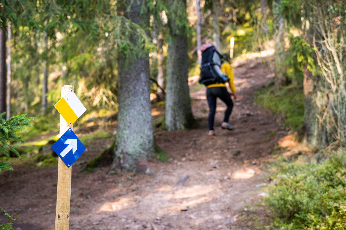 Skylt för vandringsled i förgrunden med vandrare i bakgrunden