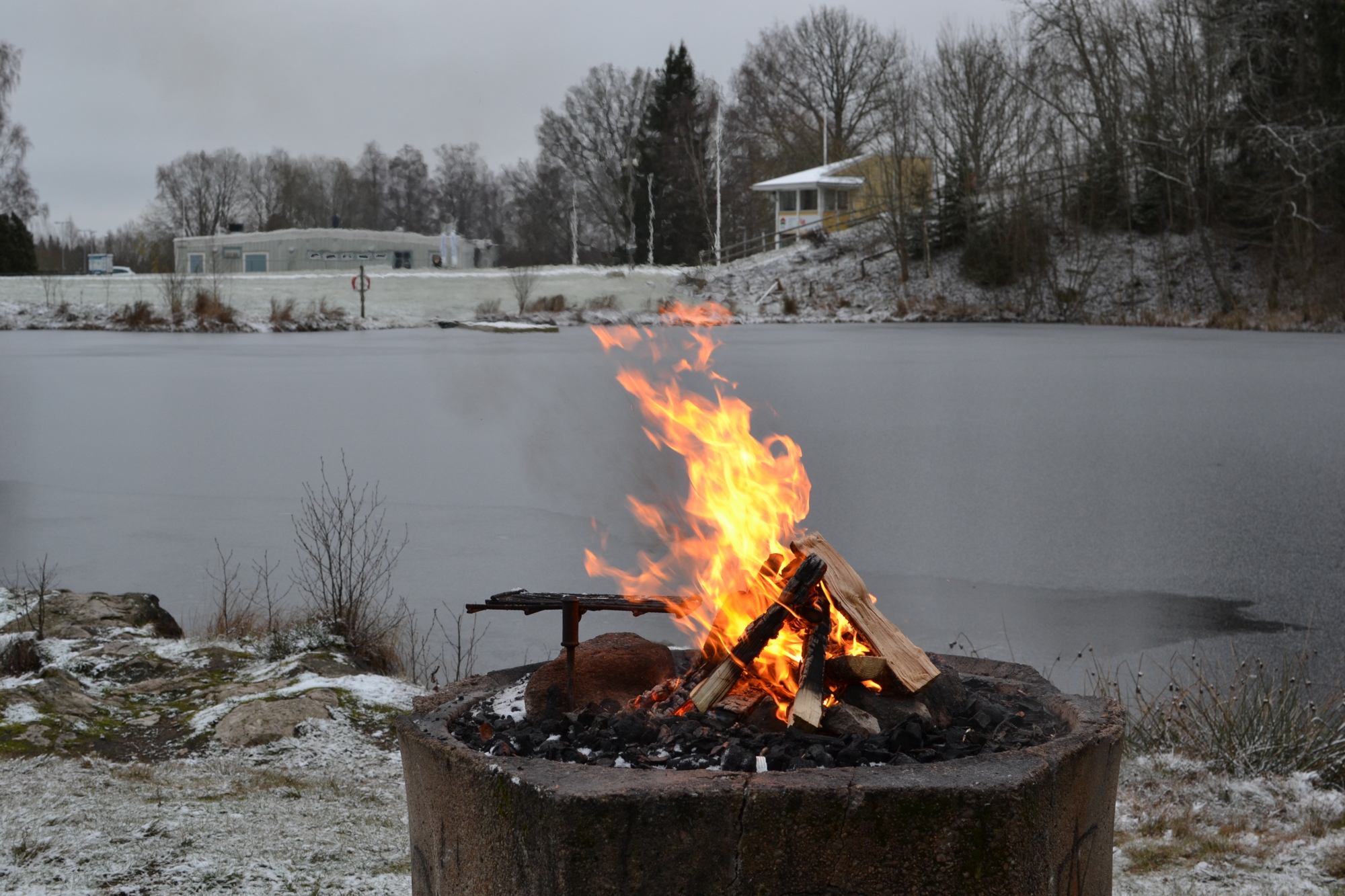 Brinnande eld på grillplats framför en sjö