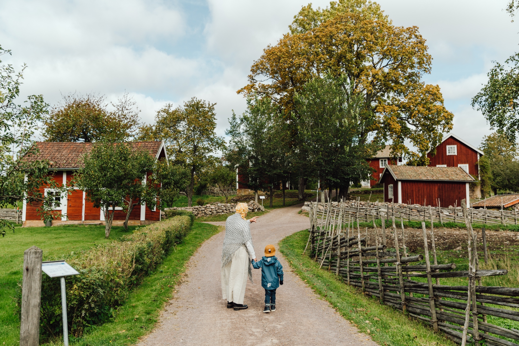Kvinna och barn som går i en äldre by med röda stugor mellan två trästaket