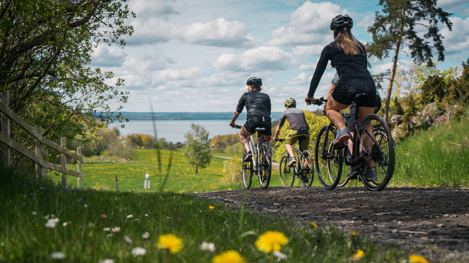 Tre personer som cyklar på en grusväg med en sjö framför dem